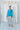 Woman in sky-blue blouse and silver skirt in minimal mirrored room