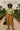 Woman in sage ribbed knit top and brown midi skirt with wide-brim hat in garden path