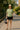 Woman in sage green ribbed top with black mini skirt and straw hat on sunny street