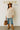Woman in white swing top, jeans, and wide-brim hat standing confidently