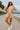Model posing on boardwalk in ash mocha fleece sweatshirt and shorts set with sneakers and cap, coastal backdrop.