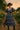 Model in tiered blue midi dress with wide belt, sunhat, and lace-up boots in garden