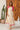 Woman wearing a cream dress with pink accents standing in front of a wooden door.