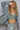 Woman wearing a denim jacket, green crop top, and patterned pants with a gray background