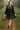 Woman in black babydoll dress with polka dots, plaid trim, tiered hem, strolling in garden, morning sunlight
