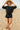 Woman in black fleece set with shorts and boat neck top, walking on sandy beach at sunrise light