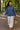 Model walking in blue indigo scuba sweatshirt with wide trousers and tan clogs, carrying straw tote, morning.