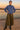 Woman posing in blue indigo scuba sweatshirt with pleated skirt and black boots, riverside at sunset glow.