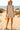 Woman in bow print mini dress with ruffle hem and espadrille wedges, standing on sand dunes near ocean