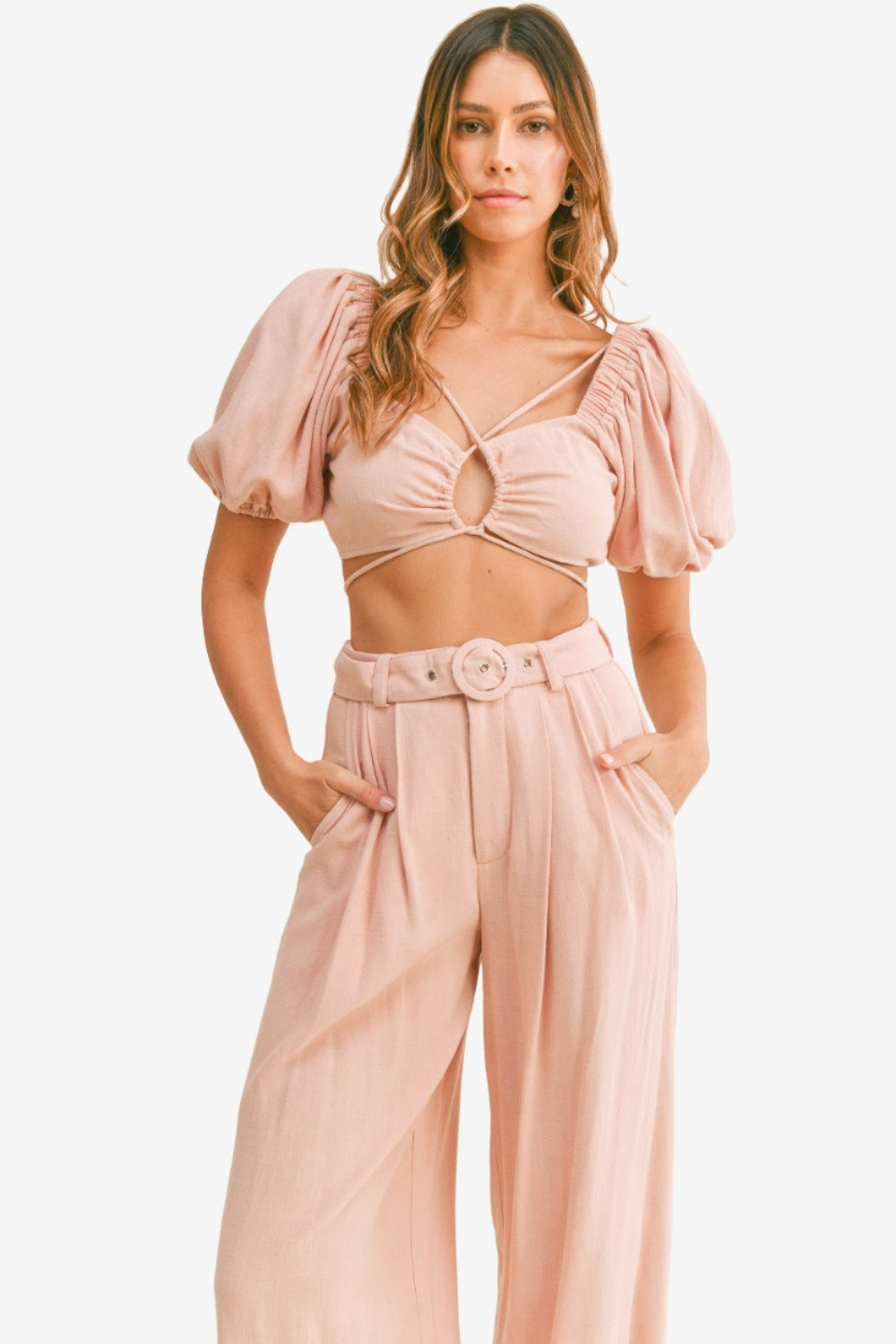 Fashion-forward woman in a cut out drawstring crop top and belted pants set, showcasing modern style.