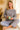 Sitting cross-legged in chenille knit sweater with striped pants and slippers, sunny indoor nook