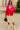 Woman in fuchsia-red blazer with cream skirt and boots holding black handbag