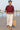 Woman strolling in merlot scallop hem shirt with white pants and straw tote, harbor background, morning sun.