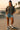 Woman in ash black oversized t-shirt, ripped denim shorts and high-top sneakers, standing at skate park during sunset