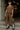 Person wearing a brown outfit with a handbag, standing on steps indoors.
