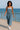 Model walking along seaside in denim wide leg overalls with silver top and sneakers, sunny day.