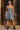Woman wearing denim mini dress with black combat boots and sunglasses, standing near rustic wooden doorway.