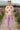 Woman in short sleeve sweater with colorful flower appliqués and lilac pants walking on a boardwalk