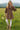 Woman in floral tie-neck babydoll dress with white leggings in meadow with mountains