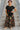 Female standing on stone steps in black flowy round hem rayon t-shirt with floral skirt and espadrilles, daytime.