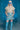 Person wearing a beige shirt, iridescent skirt, and blue knee-high boots in a blue-lit room.