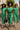 Three women in green midi dresses styled with belts, heels, scarf, hat, and handbag walking in city.