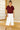Woman wearing a burgundy top and white pants in a room with wooden flooring and sliding doors.