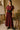 Woman in a burgundy dress standing in an art studio with easels and a chair.