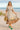 Woman in ivory printed midi dress walking along the beach with a woven bag