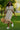 Woman in a smocked ivory midi dress walking happily through a sunny park
