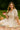 Woman in ivory midi dress holding strawberries while sitting on a picnic blanket