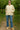 Woman in jacquard jacket with textured pattern, wearing dark jeans and boots, walking through apple orchard