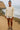 Woman in jacquard jacket and white shorts, standing near ocean cliffside trail, overcast daylight