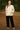 Woman in jacquard jacket with black pants and sneakers, smiling in pine forest during sunset