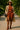 Rust knit set with trench coat and heeled booties, styled with straw hat and black crossbody