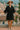 Woman in a black dress and beige hat standing on a balcony with a scenic background