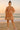 Woman in rust embroidered mini dress with tassel neckline and puff sleeves, standing on a sandy beach at sunrise in pink sneakers