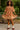 Woman wearing a brown dress with white patterns in an outdoor setting
