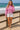 Woman in mauve acid wash hoodie, white shorts and espadrilles, standing on beach boardwalk, sunny day