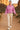 Woman in mauve acid wash hoodie, beige joggers and white sneakers, walking desert trail at sunset