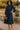 Woman in navy midi dress with ruffle shoulders, standing near stone fountain outdoors