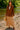 Woman in Mocha suede blazer with fringe, beige dress and sandals, standing by river, sunny day