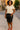Woman standing on city street in natural lace cotton shirt with black leather skirt and red heels, sunset glow.