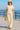 Smiling woman strolling seaside in natural lace cotton shirt with wide pants and straw hat, sunny morning.