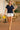 Model walking on terrace in navy lace short sleeve shirt with white shorts and yellow heels, bright day