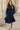 Woman in navy ruffle shoulder midi dress with red heels and floral scarf in city street