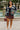 Smiling woman in navy stripe cable knit cardigan with burgundy skirt and white flats, fountain background.