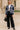 Model standing in navy stripe cable knit cardigan with black trousers and boots, city architecture backdrop