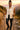 Woman hiking rocky trail at sunset in oatmeal quilted vest with leather pants and boots, holding trekking poles