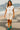 Model strolling along beach promenade in off-white ribbed sweater vest with cream shorts, cloudy morning